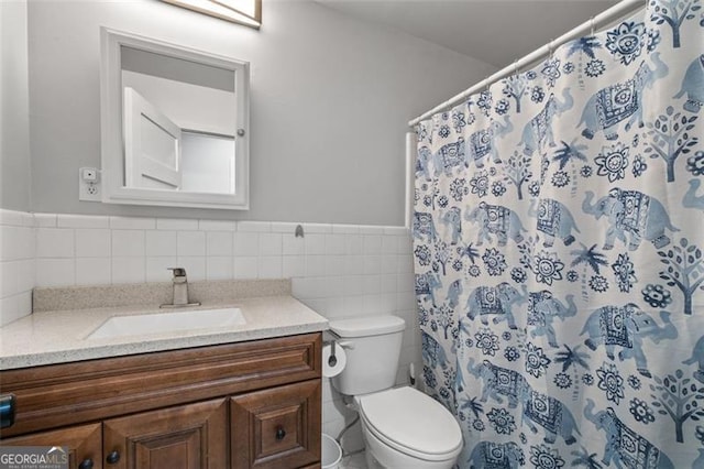 bathroom with wainscoting, toilet, curtained shower, vanity, and tile walls