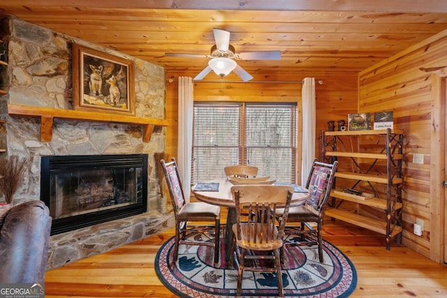 dining space with a stone fireplace, wood walls, wood-type flooring, and wood ceiling