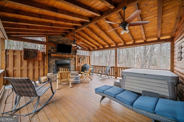 wooden deck with ceiling fan, an outdoor stone fireplace, and a hot tub