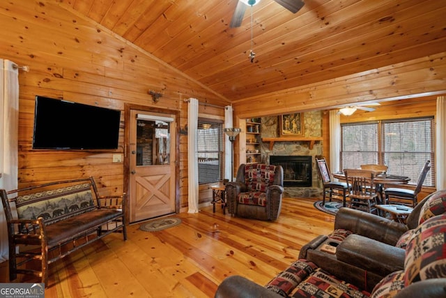 living room featuring a stone fireplace, wooden ceiling, wooden walls, a ceiling fan, and vaulted ceiling