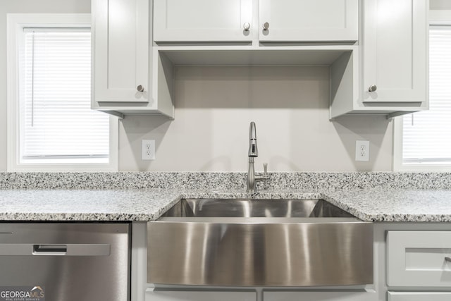 kitchen featuring stainless steel dishwasher, a sink, a wealth of natural light, and light stone countertops