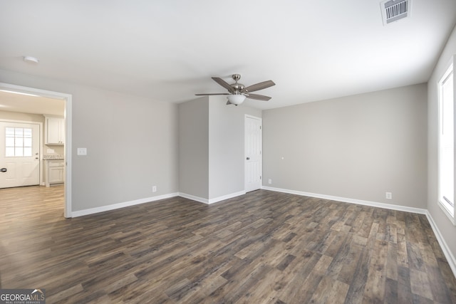 unfurnished room featuring dark wood-style floors, a ceiling fan, visible vents, and baseboards