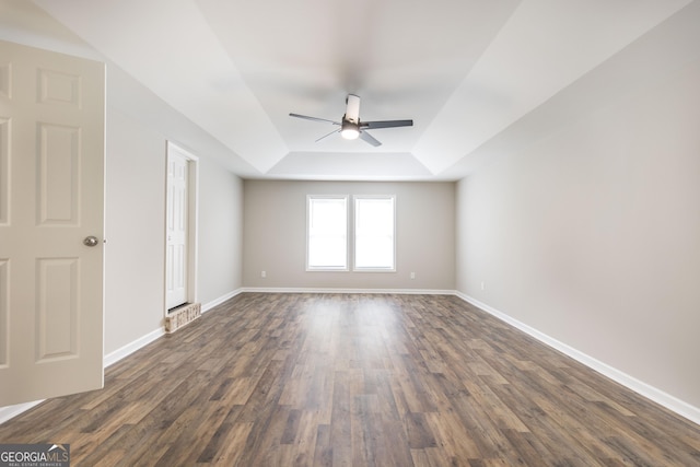 unfurnished room with baseboards, a tray ceiling, dark wood finished floors, and a ceiling fan