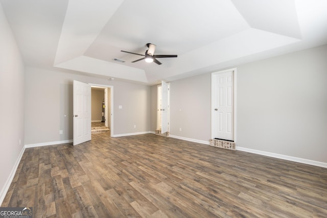 unfurnished bedroom featuring baseboards, visible vents, a raised ceiling, ceiling fan, and wood finished floors