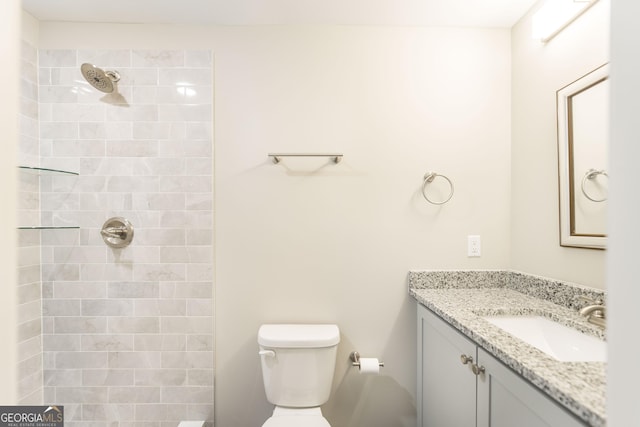 full bathroom featuring a tile shower, vanity, and toilet