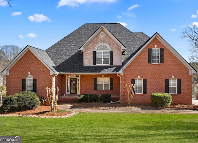 traditional-style house featuring roof with shingles, a front lawn, and brick siding