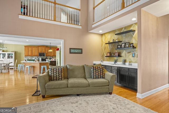 living area with recessed lighting, a towering ceiling, light wood-style flooring, and baseboards