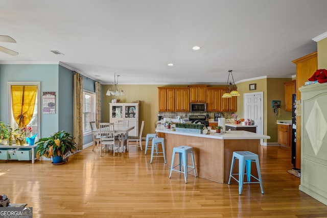 kitchen with light countertops, brown cabinets, light wood finished floors, stainless steel microwave, and a kitchen bar