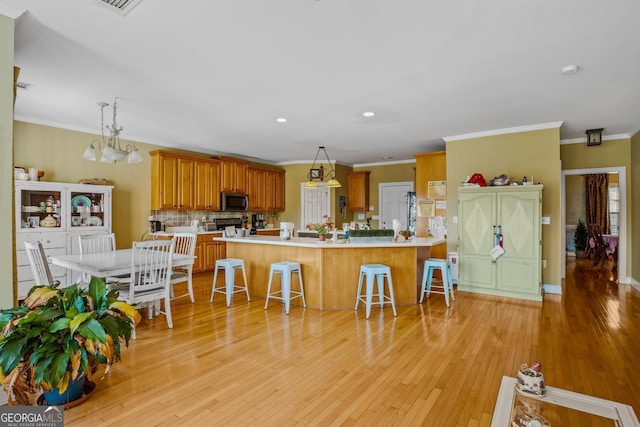 kitchen with light wood-type flooring, light countertops, stainless steel microwave, and a kitchen bar