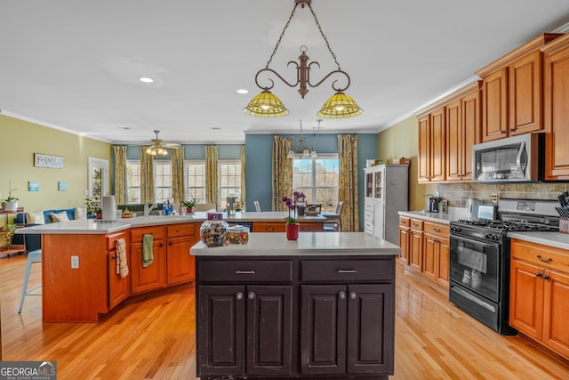 kitchen with a kitchen island, light countertops, stainless steel microwave, gas stove, and crown molding