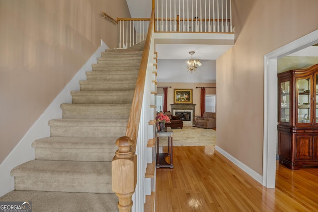 staircase featuring a high ceiling, wood-type flooring, a glass covered fireplace, and baseboards