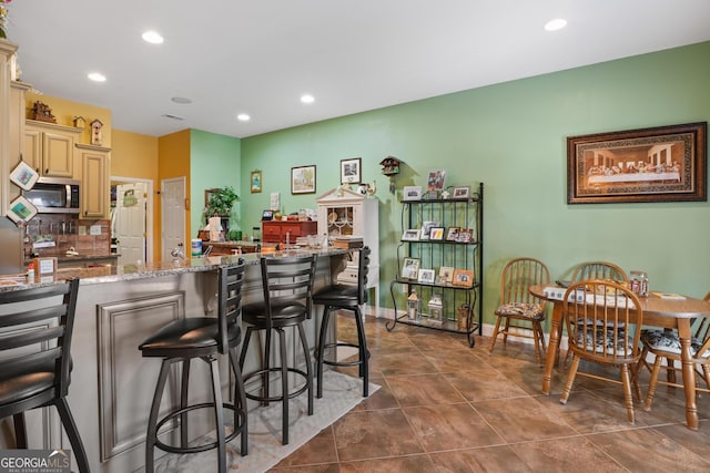 kitchen featuring cream cabinetry, stainless steel microwave, stone countertops, and a kitchen breakfast bar