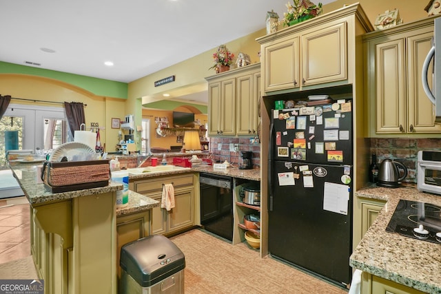 kitchen with a peninsula, a sink, cream cabinetry, decorative backsplash, and black appliances