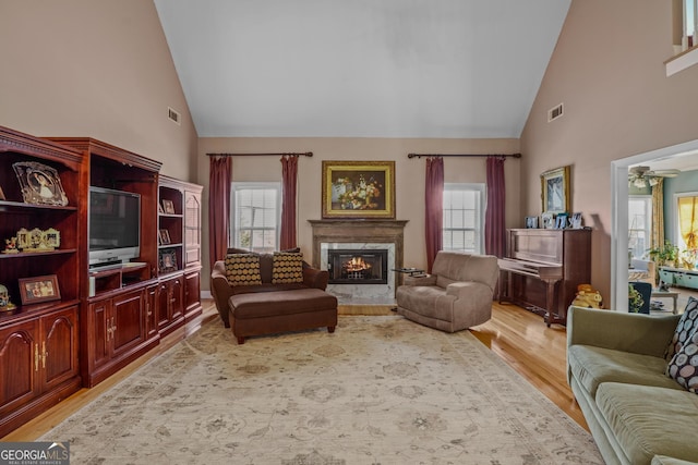 living room featuring light wood-style floors, a high end fireplace, visible vents, and high vaulted ceiling