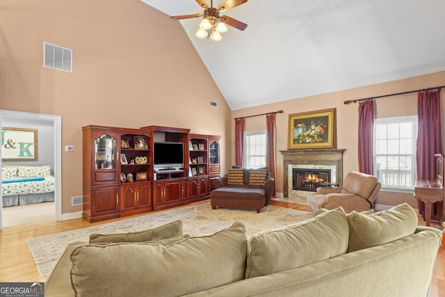 living area featuring high vaulted ceiling, a fireplace, visible vents, and wood finished floors