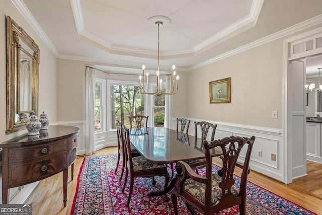 dining area featuring a chandelier, light wood-type flooring, a raised ceiling, and ornamental molding