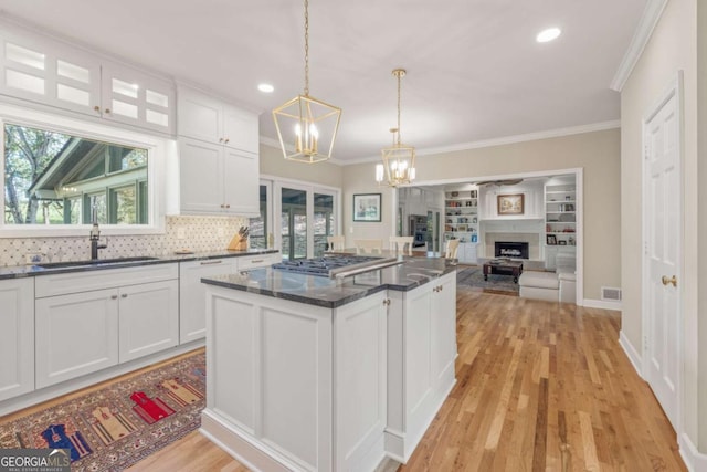 kitchen featuring a center island, a fireplace, visible vents, white cabinets, and a sink