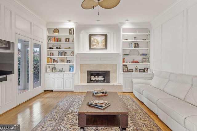 living area with light wood-style floors, built in shelves, ornamental molding, and a tiled fireplace