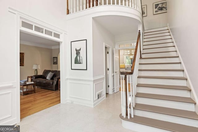 entrance foyer featuring visible vents, arched walkways, a towering ceiling, stairway, and a decorative wall