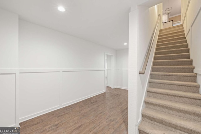 stairs with recessed lighting, wainscoting, a decorative wall, and wood finished floors