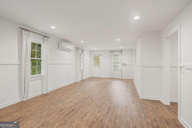 unfurnished room featuring a wall unit AC, wood finished floors, a wealth of natural light, and recessed lighting