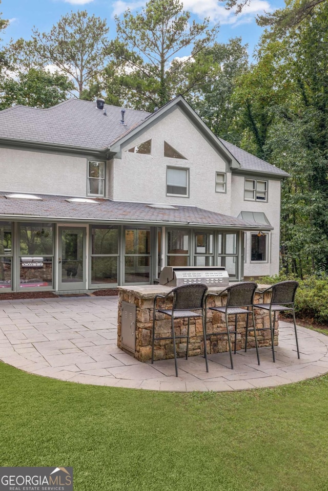 back of house featuring stucco siding, outdoor dry bar, a lawn, and a patio