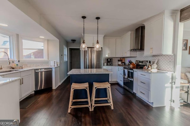 kitchen with a sink, appliances with stainless steel finishes, wall chimney range hood, a center island, and dark wood-style floors