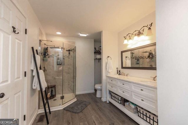 bathroom featuring double vanity, toilet, a stall shower, a sink, and wood finished floors