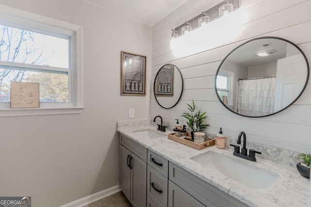 full bath with double vanity, tile patterned flooring, a sink, and baseboards