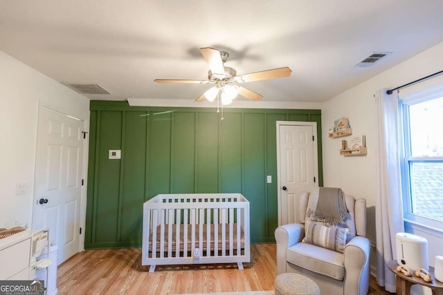 bedroom with light wood-type flooring, a nursery area, visible vents, and a closet