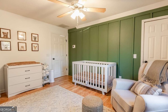 bedroom featuring a nursery area, ceiling fan, and light wood finished floors