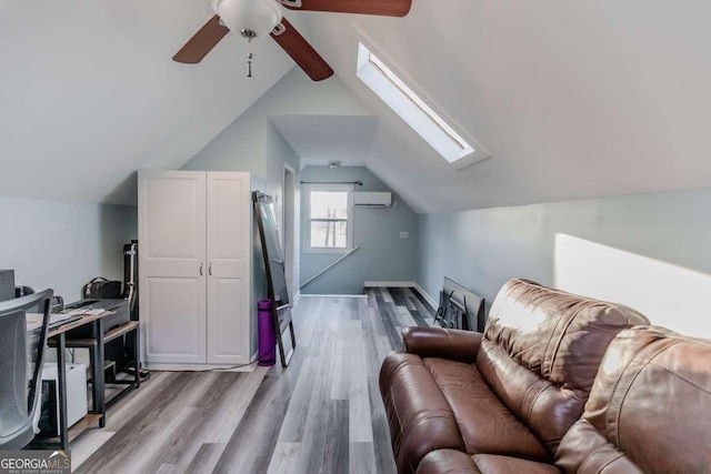 additional living space featuring ceiling fan, vaulted ceiling with skylight, light wood finished floors, and a wall mounted air conditioner