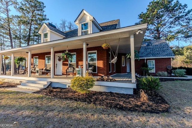 back of house featuring a porch, roof with shingles, and brick siding