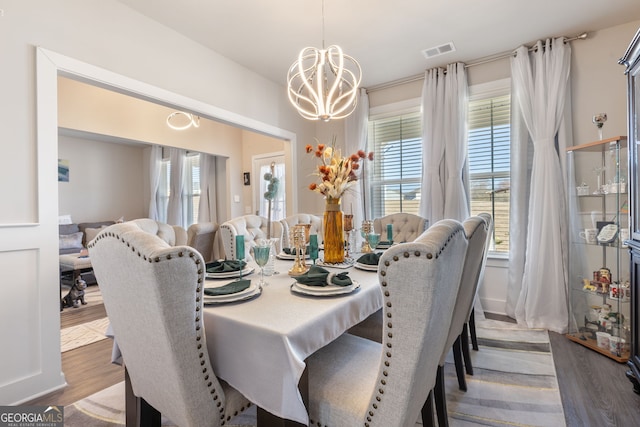 dining room featuring visible vents, a healthy amount of sunlight, wood finished floors, and an inviting chandelier