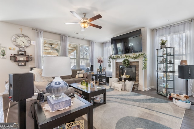 living area featuring wood finished floors, baseboards, visible vents, ceiling fan, and a glass covered fireplace