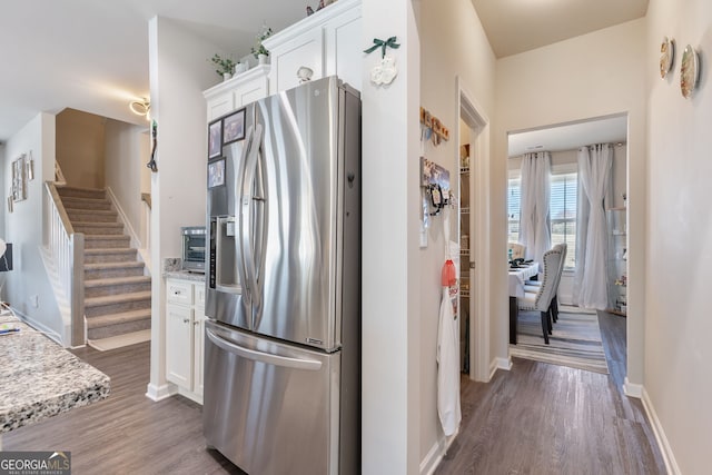 kitchen with white cabinets, wood finished floors, stainless steel refrigerator with ice dispenser, and baseboards