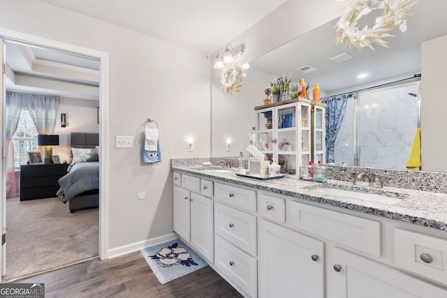 ensuite bathroom featuring double vanity, wood finished floors, tiled shower, and a sink