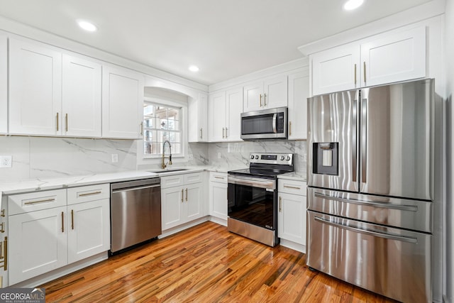 kitchen with decorative backsplash, stainless steel appliances, light wood-type flooring, white cabinetry, and a sink