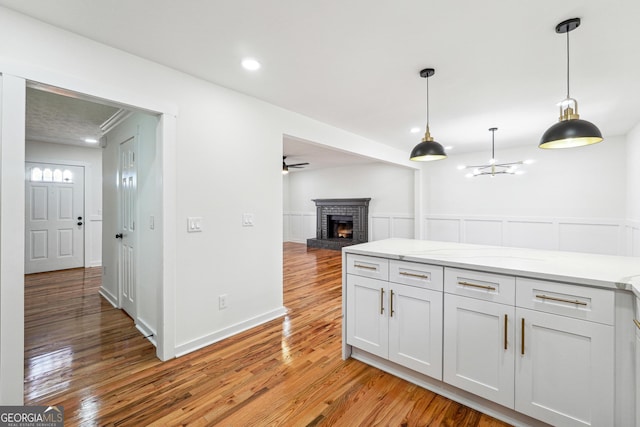 kitchen with pendant lighting, light wood-style floors, a brick fireplace, open floor plan, and light stone countertops