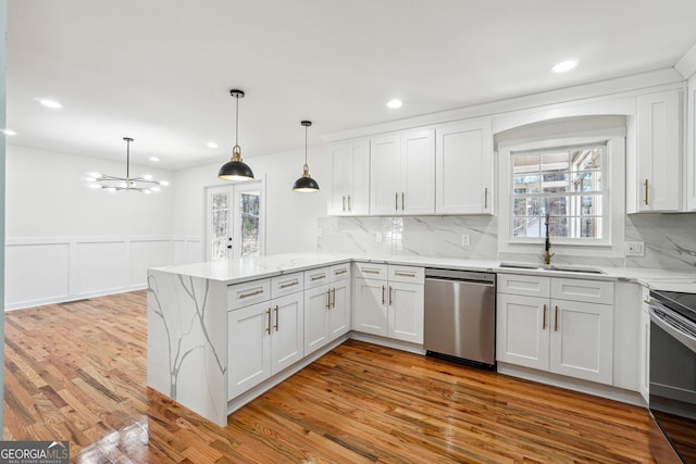 kitchen featuring a peninsula, a sink, white cabinets, light wood-style floors, and stainless steel dishwasher