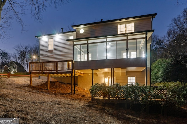 back of house at twilight with a wooden deck and a sunroom