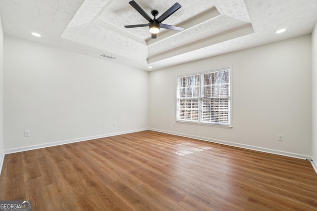 unfurnished room with a raised ceiling, ceiling fan, a textured ceiling, wood finished floors, and baseboards