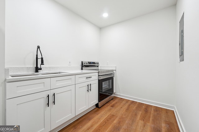 kitchen featuring a sink, baseboards, white cabinets, light wood-type flooring, and stainless steel electric range oven