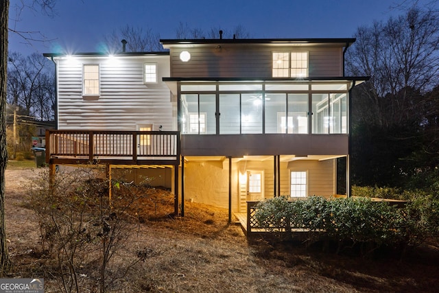 back of house at twilight featuring a sunroom and a wooden deck