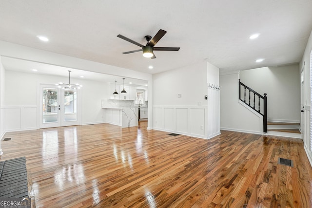 unfurnished living room featuring visible vents, a decorative wall, light wood-style floors, a ceiling fan, and stairs