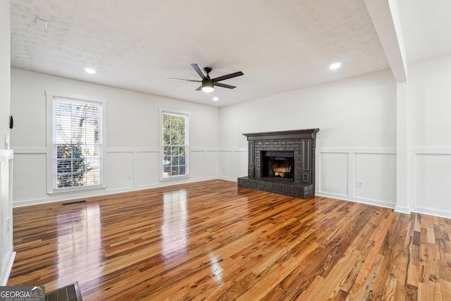 unfurnished living room featuring a brick fireplace, a ceiling fan, visible vents, and wood finished floors