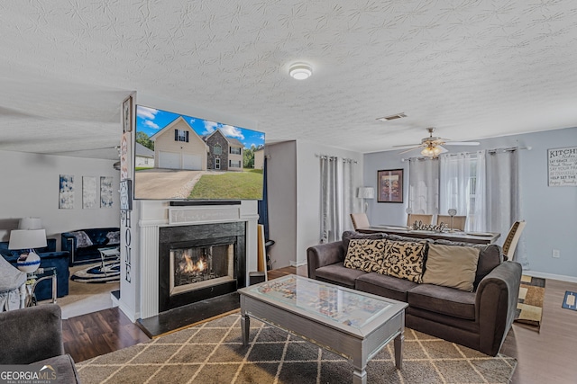 living area featuring visible vents, a premium fireplace, a textured ceiling, wood finished floors, and baseboards