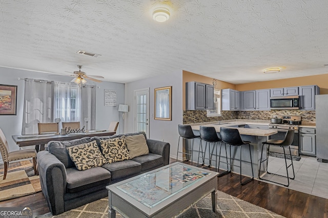 living room with a textured ceiling, light wood-type flooring, visible vents, and a ceiling fan