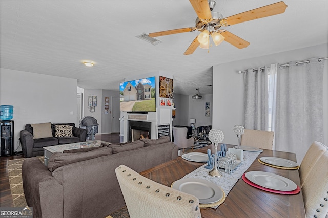 dining area with a warm lit fireplace, wood finished floors, visible vents, and a ceiling fan