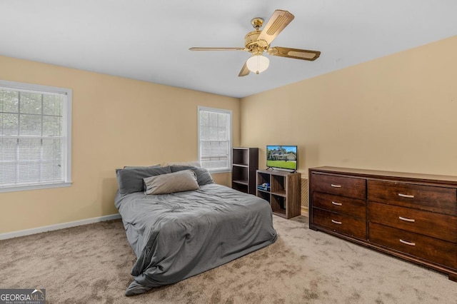 bedroom featuring light carpet, multiple windows, baseboards, and a ceiling fan